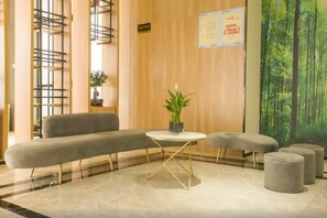 A modern lobby with a sofa, a small round table with a plant, and a mural of a forest. - Greentree Inn Taizhou Jiangyan Hardware City Expre (Taizhou)