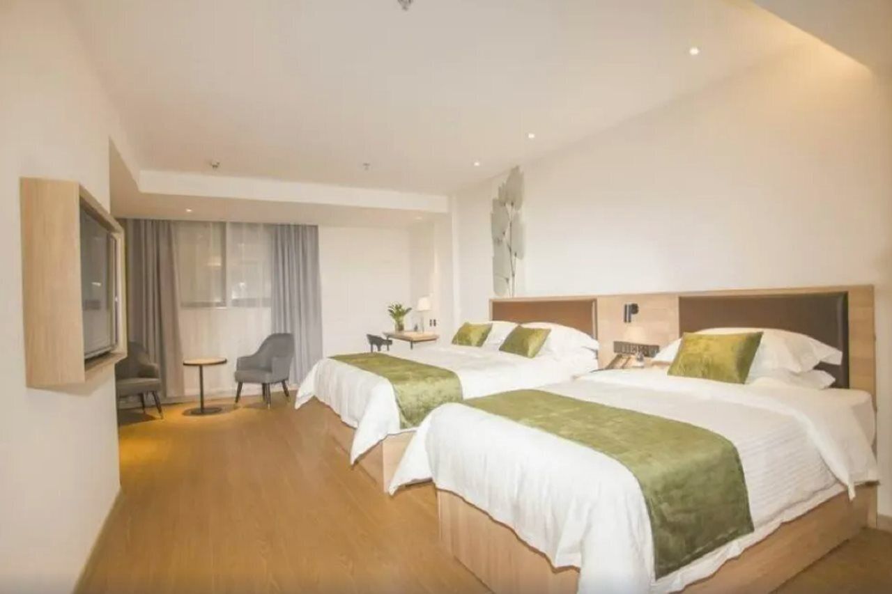 A hotel room with two beds, a small desk, a chair, and a window with curtains.