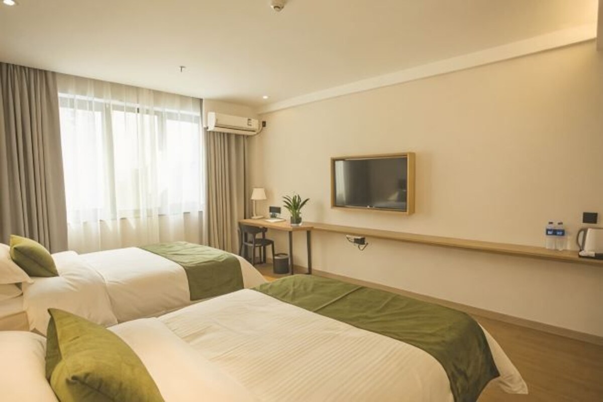 A hotel room with two beds, a desk with a chair, a TV, and a shelf with water bottles.