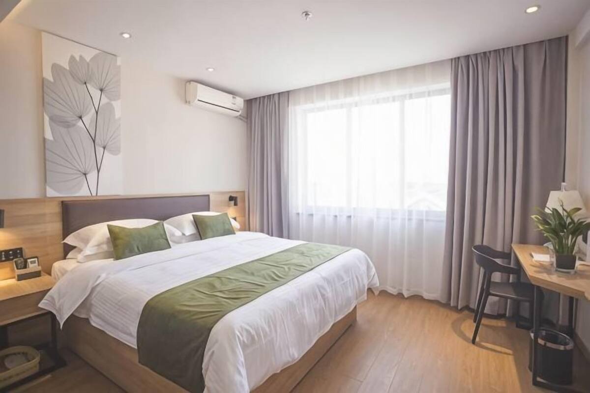 Een hotelkamer met een bed, nachtkastje, lamp en een raam met gordijnen.