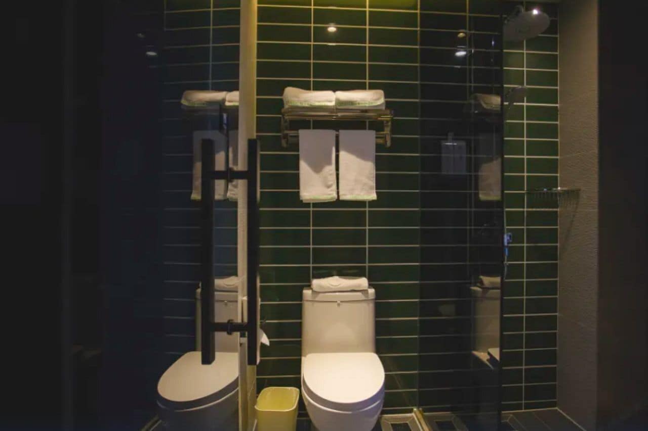 A bathroom with two toilets, a shower, and a towel rack.