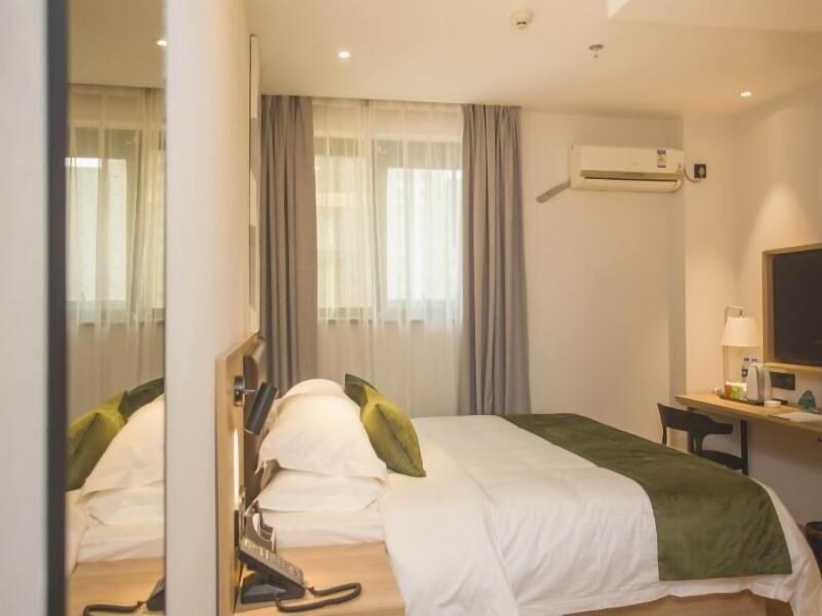 A hotel room with a bed, a desk, an air conditioning unit, and a mirror.