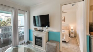 Une pièce avec une cheminée, un téléviseur fixé au-dessus, un lit avec une table de chevet et une table en verre avec des chaises à l’extérieur.