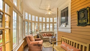 A sunroom with large windows, a ceiling fan, a welcome sign, and a bench with a 'gather together' pillow. - Free WiFi Home w/ Balcony & Yard in Surgeon Bay (Sturgeon Bay)