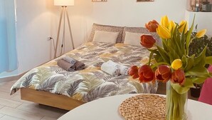 Et soveværelse med seng, sengetår, blomster i en vase og billedkunst på væggen.