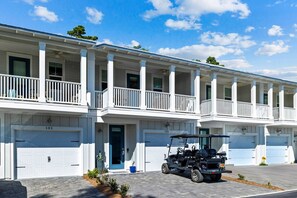 A multi-story residential building with white exterior, multiple garage doors, and a golf cart parked in front.