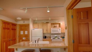 Une cuisine avec des meubles en bois, un îlot central doté de tabourets, un réfrigérateur, un four à micro-ondes et une cuisinière.