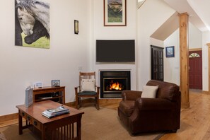 A living room with a fireplace, a television, a brown leather sofa, a wooden chair, and a table with magazines.