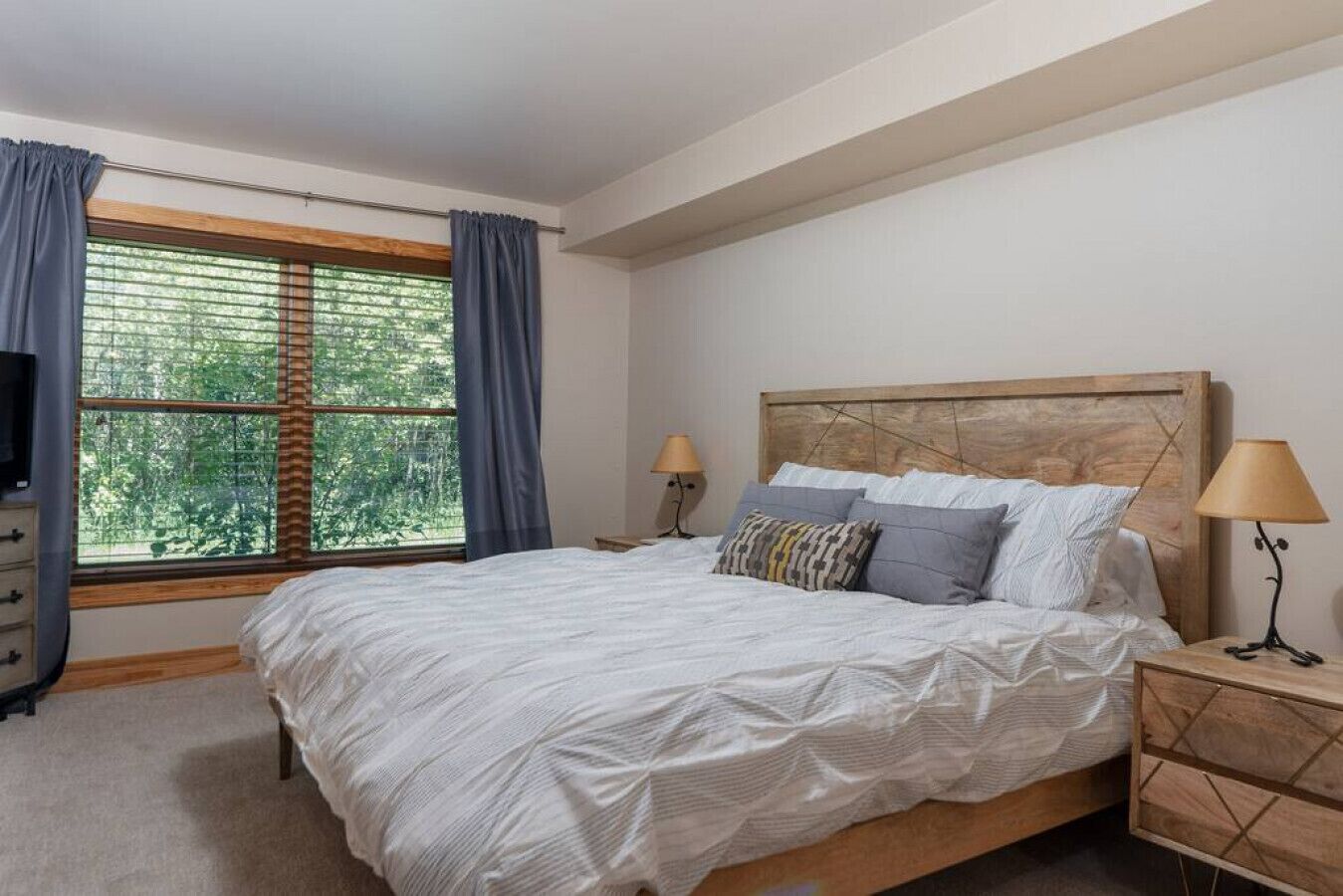 Ein Schlafzimmer mit einem großen Bett, zwei Nachttischen, einem Fernseher und einem Fenster mit Vorhängen.