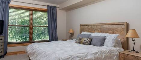 Ein Schlafzimmer mit einem großen Bett, zwei Nachttischen, einem Fernseher und einem Fenster mit Vorhängen.