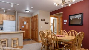 Een kleine keuken met houten keukenkastjes, een koelkast en een eethoek met een ronde tafel en houten stoelen.