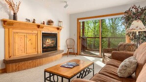 A living room with a fireplace, a sofa, a coffee table, and a large sliding glass door leading to an outdoor deck.