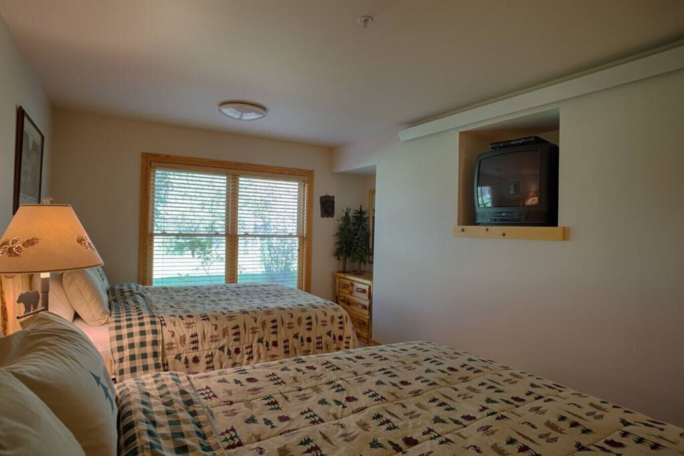 A bedroom with two beds, a TV on the wall, and a window with blinds.