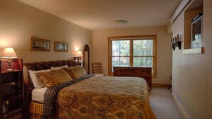 Une chambre à coucher avec un grand lit, une table de chevet, une commode et une fenêtre donnant sur les arbres.