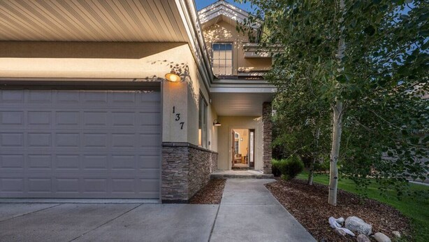 A two-story house with a garage, a stone base, and a well-maintained lawn. - Alpine Meadows: Creekside, Aspen Views, Light & Spacious, Fireplace & 2-car garage (Driggs)