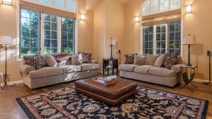 A spacious living room with two sofas, a coffee table, and a patterned rug. Large windows with blinds provide natural light. - Alpine Meadows: Creekside, Aspen Views, Light & Spacious, Fireplace & 2-car garage (Driggs)