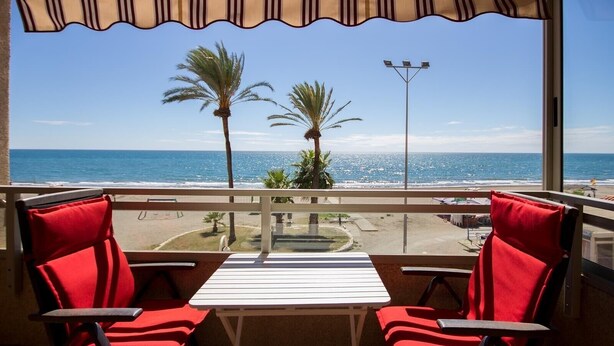 A balcony with two red chairs, a white table, and a view of the ocean and beach. - Apartment "Studio 2 Sea front" At the Beach with Sea View (Rincón de la Victoria)