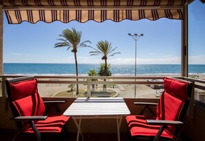 Een balkon met twee rode stoelen, een witte tafel en uitzicht op zee en strand.