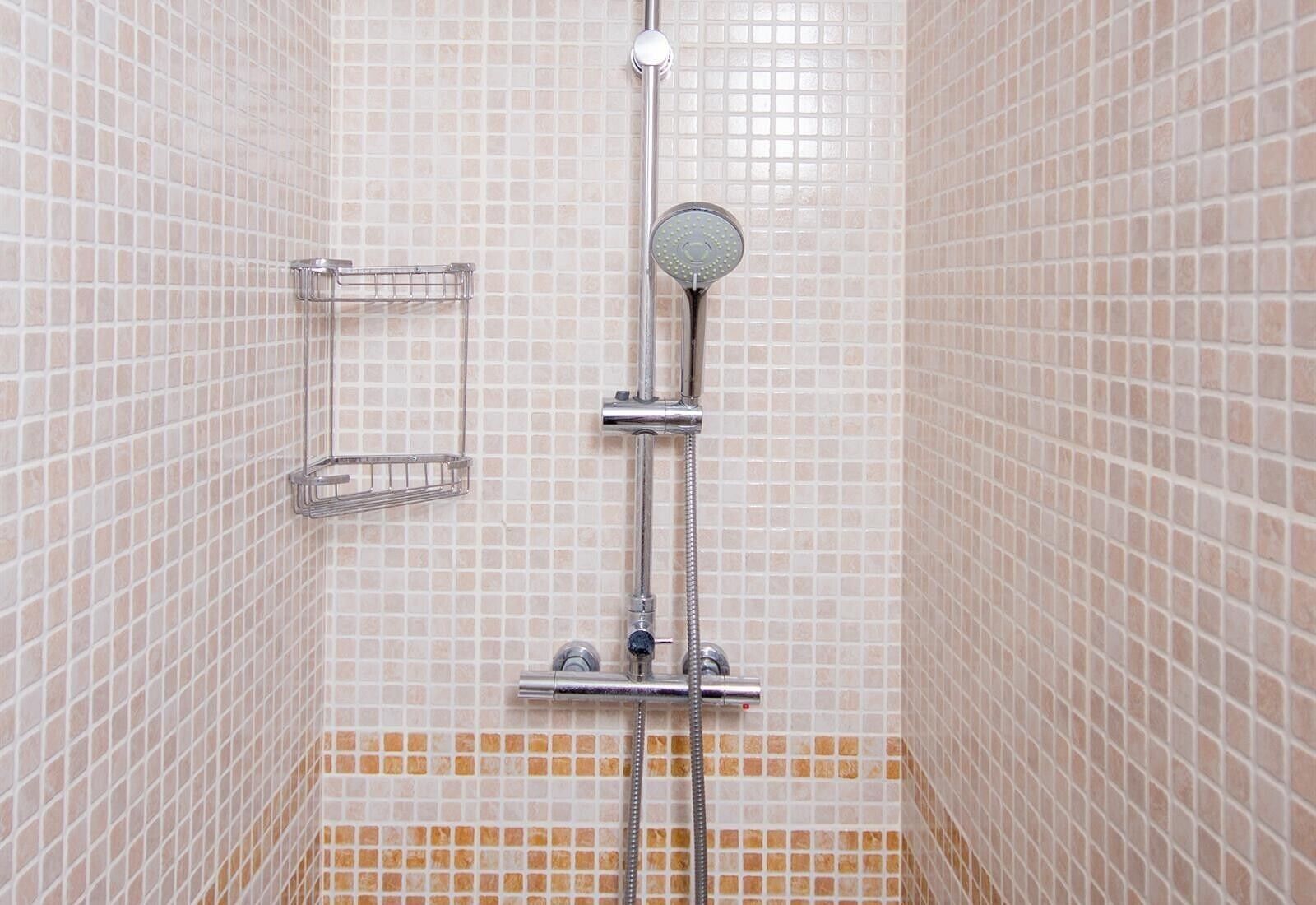 Une douche équipée d’un pommeau de douche à main, d’un porte-serviettes mural et d’un sol carrelé dont une partie est recouverte d’un carrelage d’une couleur différente.