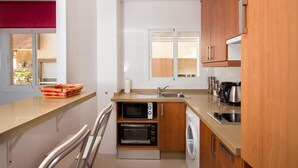 A compact kitchen with a microwave, oven, and washing machine, wooden cabinets, and a window with blinds. - Apartment "Studio 2 Sea front" At the Beach with Sea View (Rincón de la Victoria)