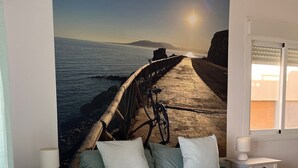 A bedroom with a bed, a nightstand, a lamp, a wall-mounted shelf, and a window. - Apartment "Studio 2 Sea front" At the Beach with Sea View (Rincón de la Victoria)