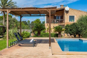 A poolside area with lounge chairs, a pergola, and a stone building with a balcony. - Vacation Home 'Cas Casai' with Mountain View, Pool & Wi-Fi (Son Negre)