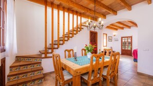 A dining area with a wooden table and chairs, a staircase with patterned steps, and a chandelier. - Vacation Home 'Cas Casai' with Mountain View, Pool & Wi-Fi (Son Negre)