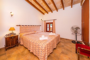 Une chambre à coucher avec un lit, une table de chevet avec une lampe, un ventilateur et une chaise en bois.