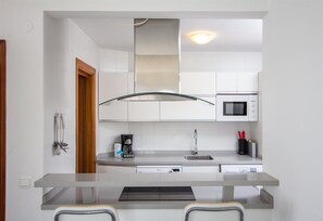 A compact kitchen with white cabinets, a microwave, a coffee maker, and a glass-top island with two chairs.