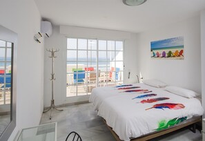 A bedroom with a large bed, a view of the beach, and a painting of colorful chairs.