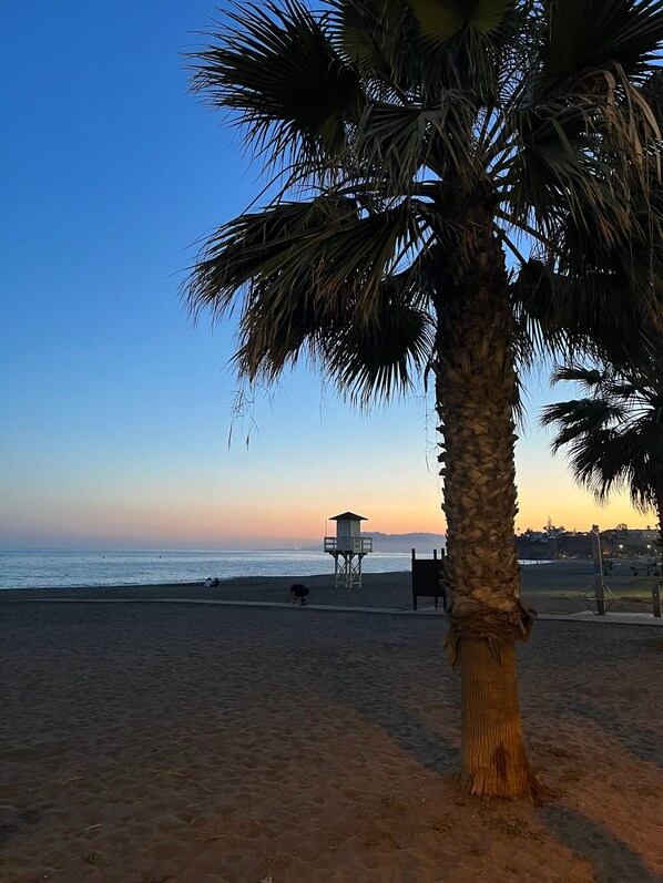 A beach with a lifeguard tower, palm trees, and a clear sky.