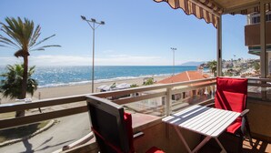 Un balcón con vistas a la playa y al océano, una mesa y sillas rojas.