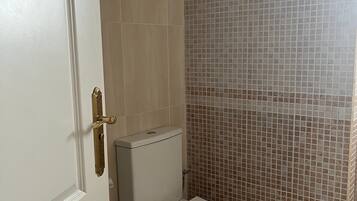 Une salle de bain équipée de toilettes, d’une poubelle et d’un espace douche.