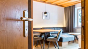 Una puerta de madera con un ojo de cerradura y un pomo, que da a un cuarto con una mesa de comedor, sillas y un sofá.