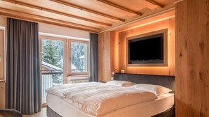 Un dormitorio con una cama grande, un televisor montado en la pared y un ventanal con cortinas.