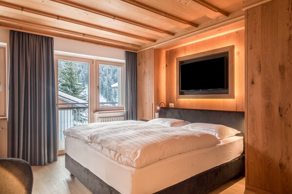 A bedroom with a large bed, a TV mounted on the wall, and a window with curtains.