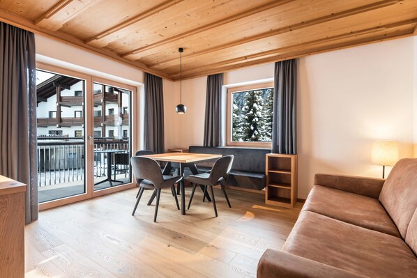Un intérieur moderne avec un plafond en bois, un coin repas comprenant une table et des chaises, un canapé et une fenêtre donnant sur un immeuble et des arbres.