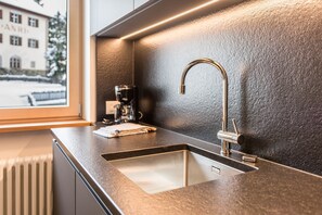 A modern kitchen with a stainless steel sink, a coffee machine, and a textured wall.