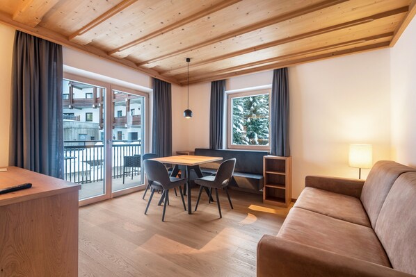 Une pièce avec un plafond en bois, un canapé, une table avec des chaises, une lampe et de grandes fenêtres avec des rideaux.