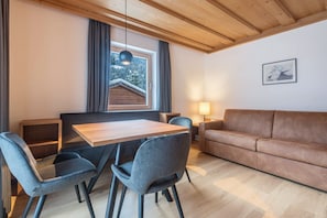 Un intérieur moderne avec une table à manger en bois, des chaises à revêtement gris, un canapé marron et une fenêtre donnant sur un paysage enneigé.