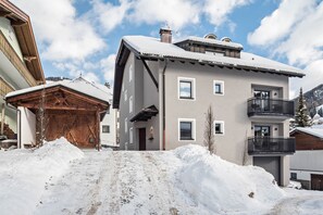 A multi-story building with a snow-covered roof, a balcony, and a wooden structure adjacent to it.