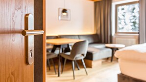A wooden door with a keyhole, a dining area with a table and chairs, a sofa, and a window with a view.