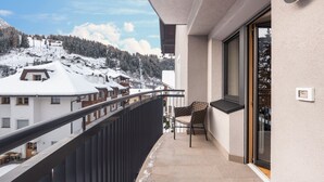 A balcony with a chair, a view of snow-covered houses, and a mountain in the background.