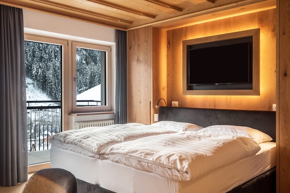 A bedroom with a bed, a TV mounted on the wall, and a window with a view of trees.
