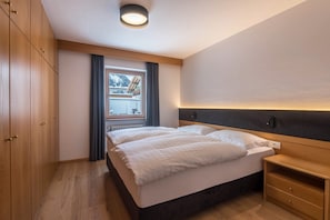 A bedroom with a bed, wooden wardrobe, and a window with curtains.