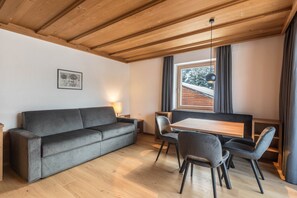 A modern interior with a wooden ceiling, a grey sofa, a dining table with chairs, and a window with curtains.