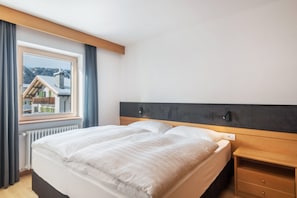 A bedroom with a bed, a nightstand, a window, and a view of buildings outside.