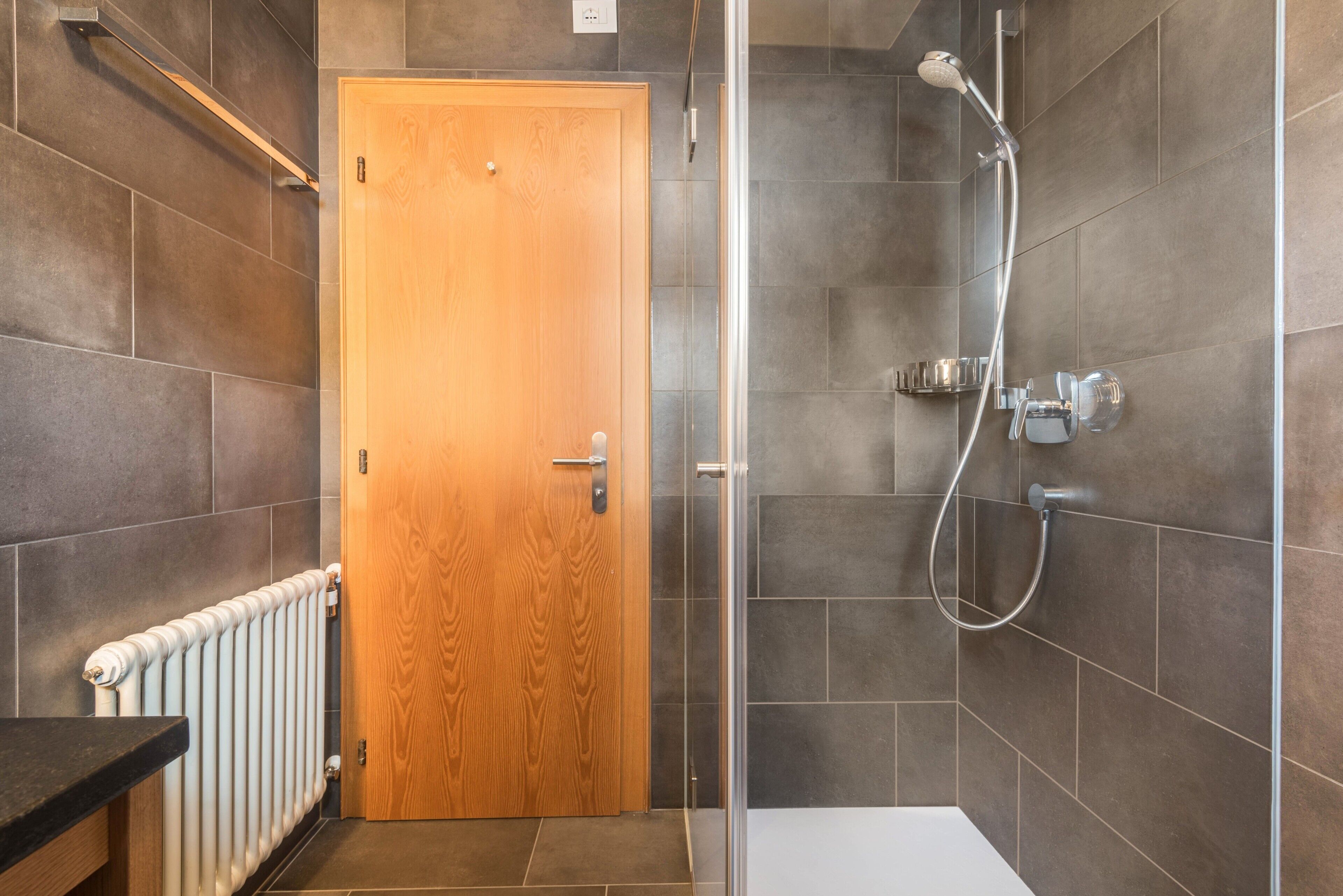 Eine Dusche mit Handbrause, Glastür und einer weißen Badewanne.