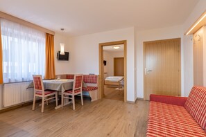 A room with a dining table, chairs, a sofa, a bed, and a wooden door.