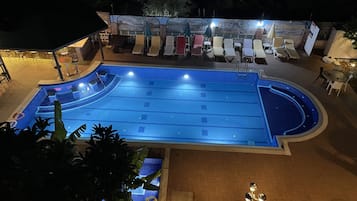 A swimming pool with lounge chairs and umbrellas, surrounded by a landscaped area with potted plants and a wooden deck.